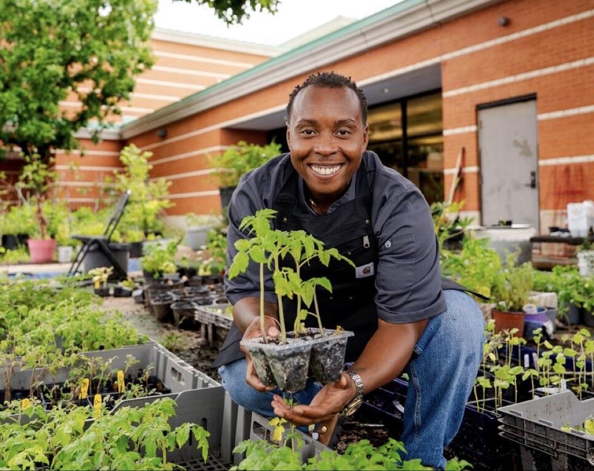 Founder Aubrey McCoy kneeling in a community garden with a tray of seedlings